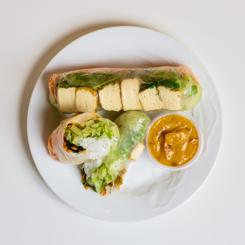 Plate of tofu-filled fresh spring rolls with vegetables, rice, and peanut dipping sauce.
