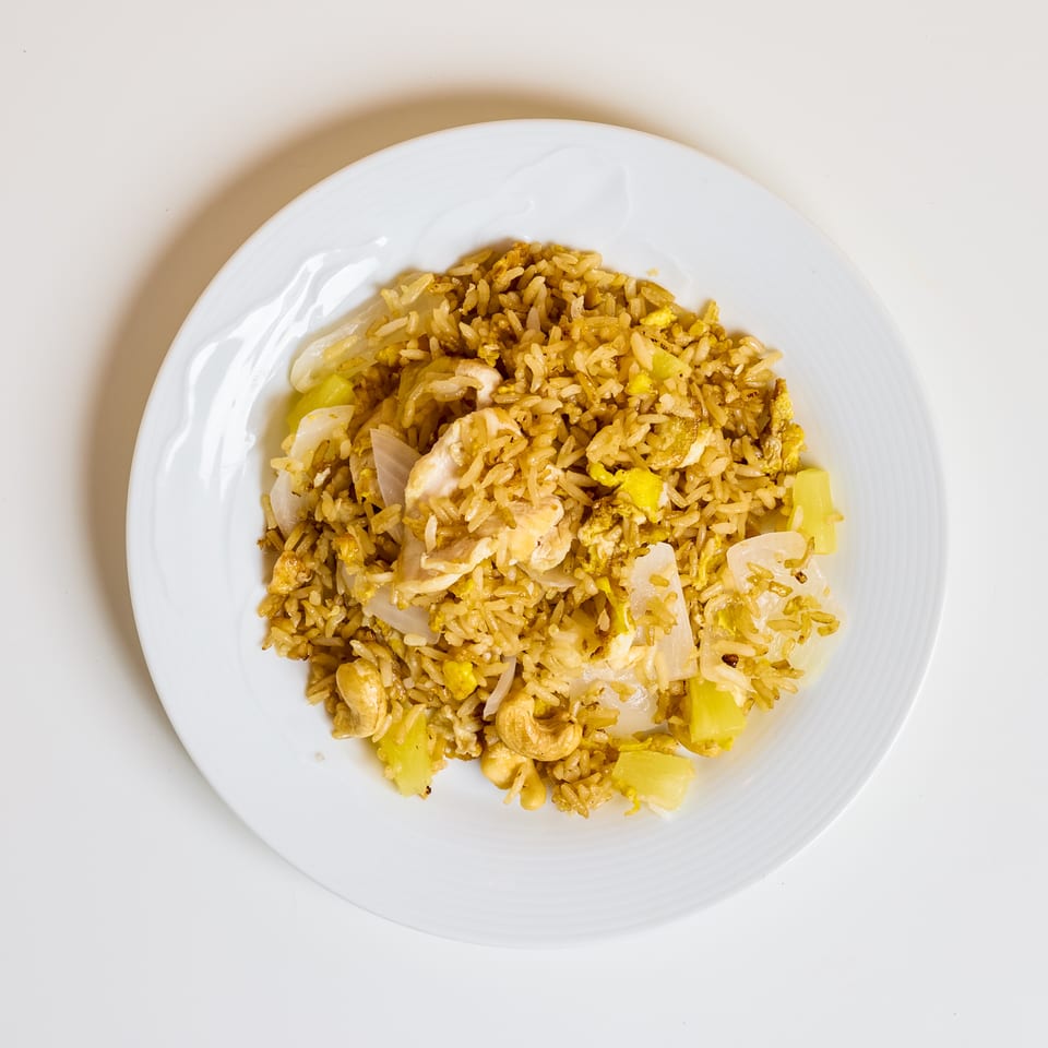 Overhead view of golden fried rice with chicken, onions, pineapple, cashews, and scrambled egg on a white plate.