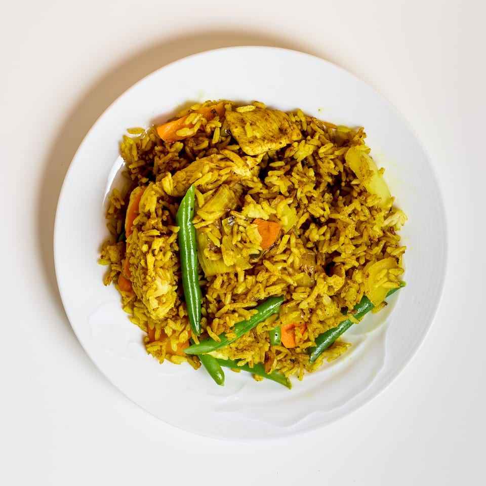 Plate of yellow spiced rice with chicken, carrots, green beans, peppers, and onions.