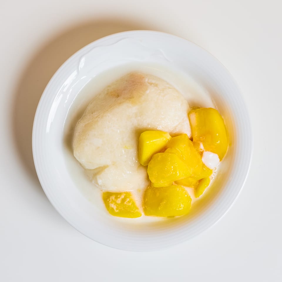 White rice topped with bright yellow mango pieces and creamy coconut sauce in a white bowl.