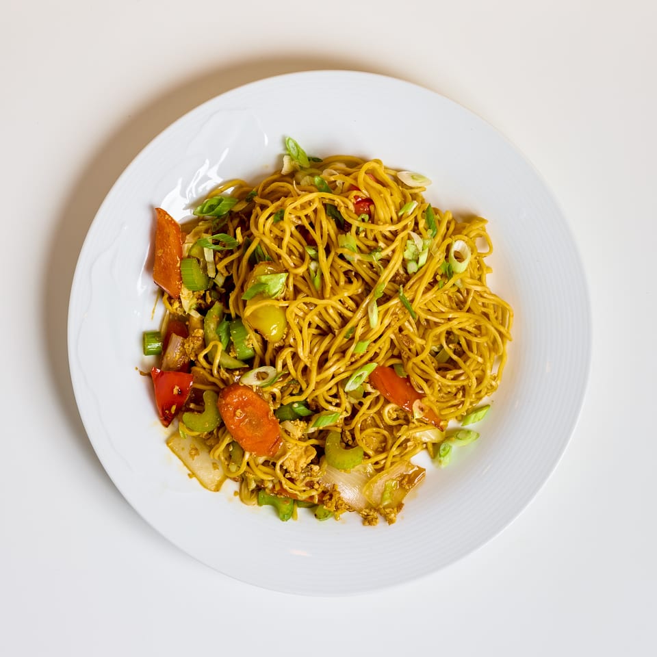 Stir-fried yellow noodles with mixed vegetables and green onions served on a white plate.