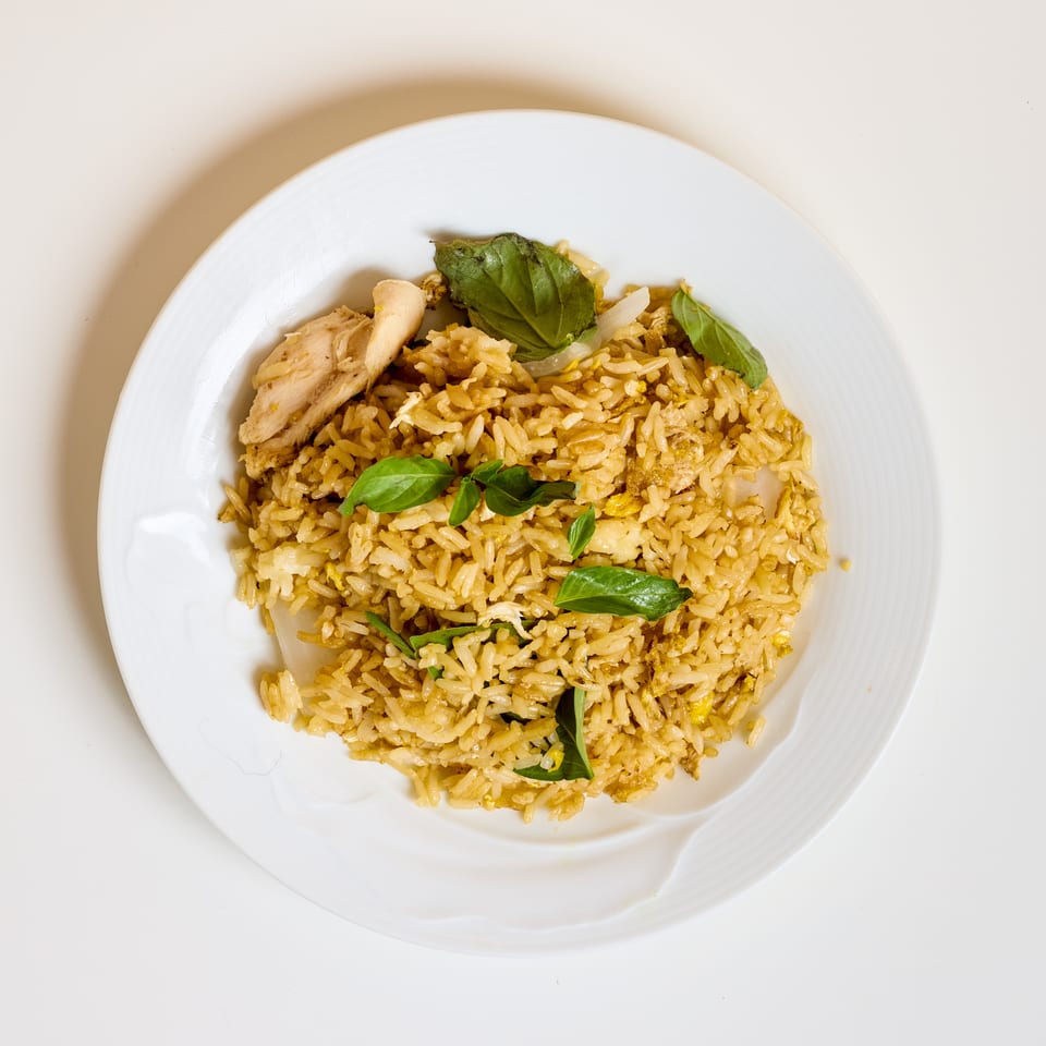 Plate of golden chicken fried rice garnished with fresh basil leaves.