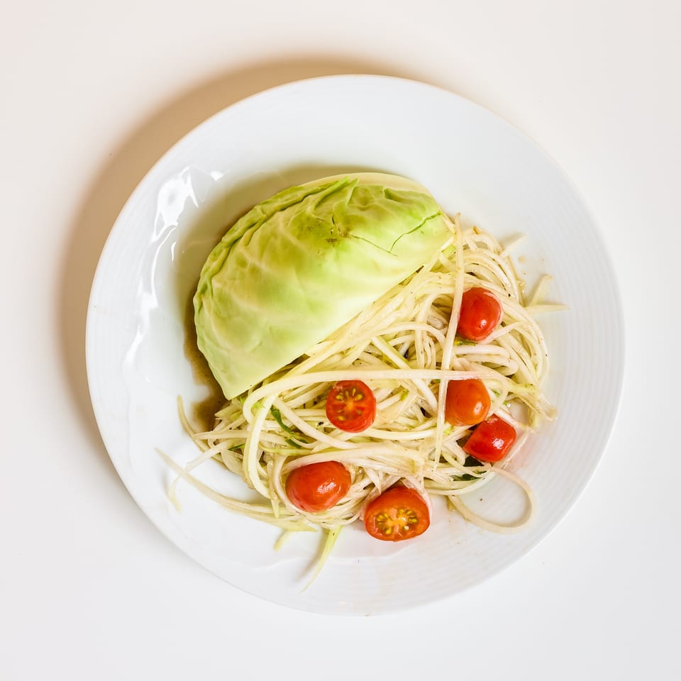 Plate of spaghetti with cherry tomatoes and a wedge of cabbage, photographed from above.