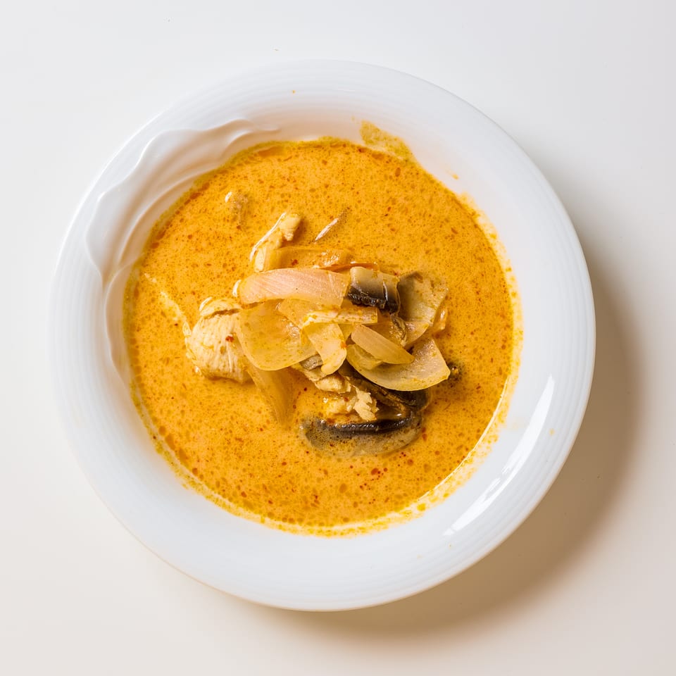 Overhead view of chicken and mushrooms in a creamy orange curry sauce on a white plate.