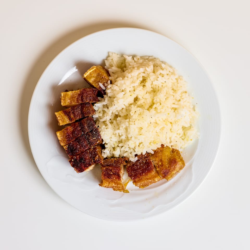 Plate of seasoned white rice with pieces of crispy grilled meat and fried tofu.
