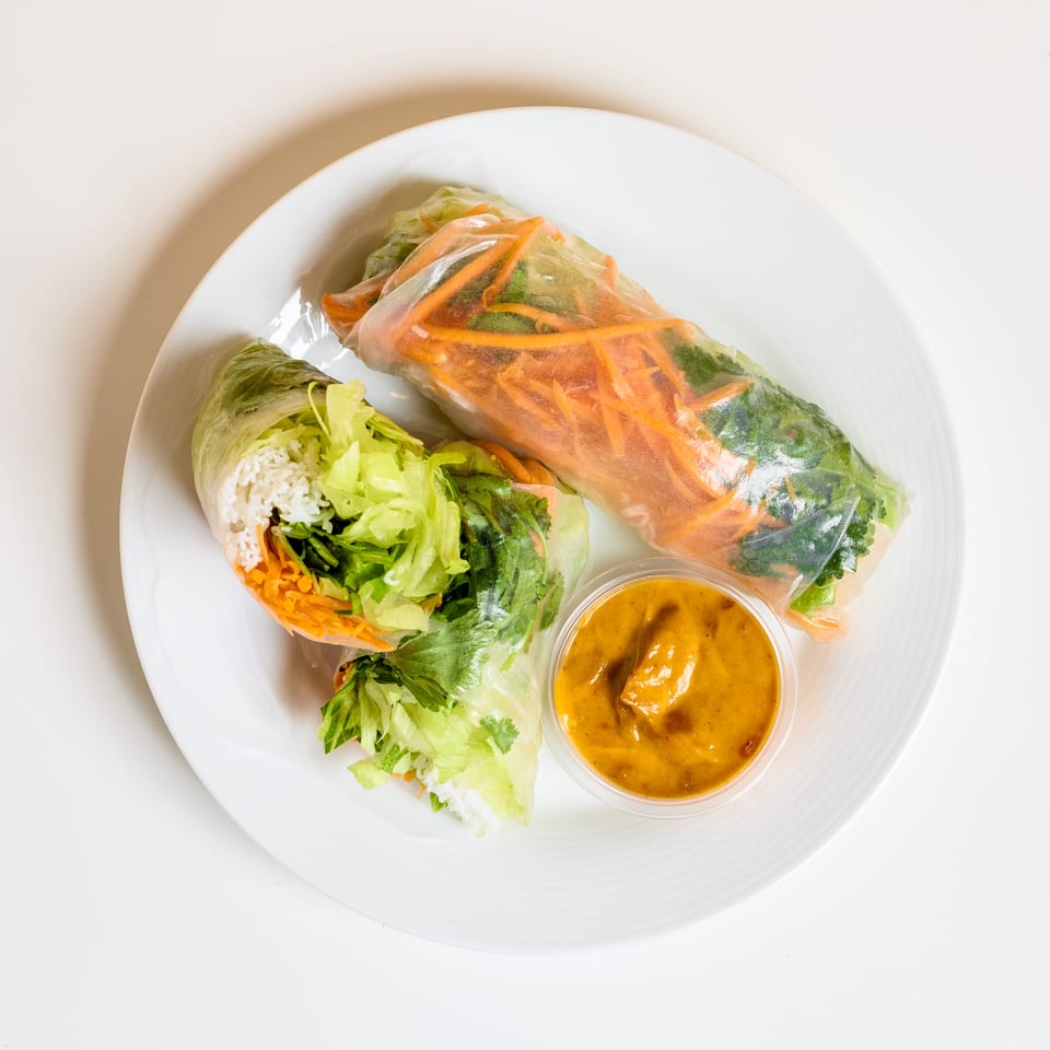 Fresh Vietnamese spring rolls filled with rice, lettuce, herbs, and vegetables, served with peanut dipping sauce on a white plate.