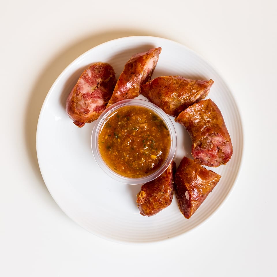 Sliced golden-brown sausage pieces arranged around a cup of chunky dipping sauce on a white plate.