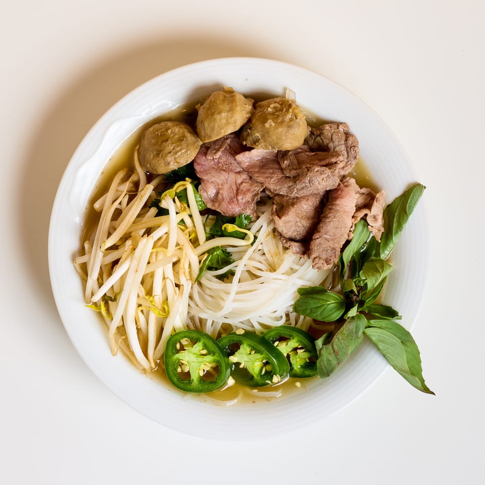 Vietnamese beef noodle soup topped with meatballs, bean sprouts, herbs, sliced jalapeños, and fresh basil.
