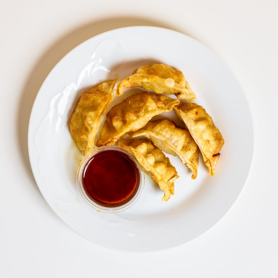 Golden fried dumplings arranged on a white plate with a small bowl of red dipping sauce.