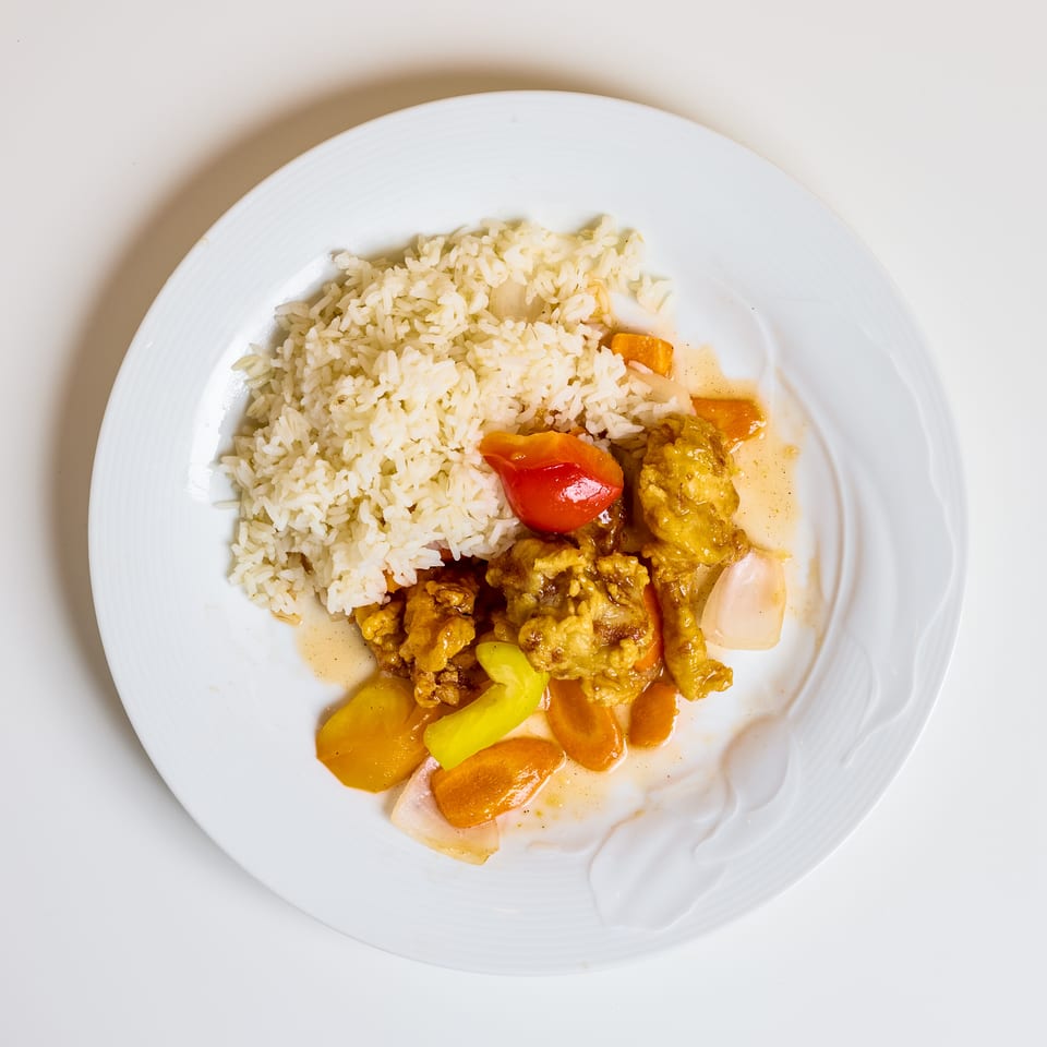 White plate of rice served with saucy golden meat and colorful vegetables, including peppers, carrots, and onions.