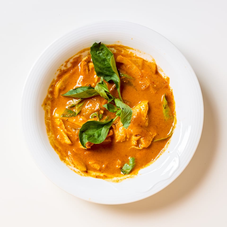 Creamy orange curry with sliced chicken, green peppers, and fresh basil served on a white plate.
