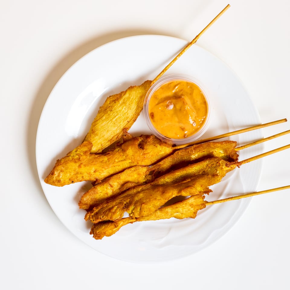 Golden grilled chicken skewers served on a white plate with a cup of creamy orange dipping sauce.