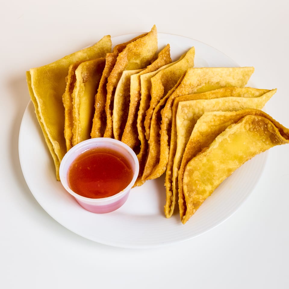 Golden fried triangular pastries arranged on a white plate with a cup of red dipping sauce.